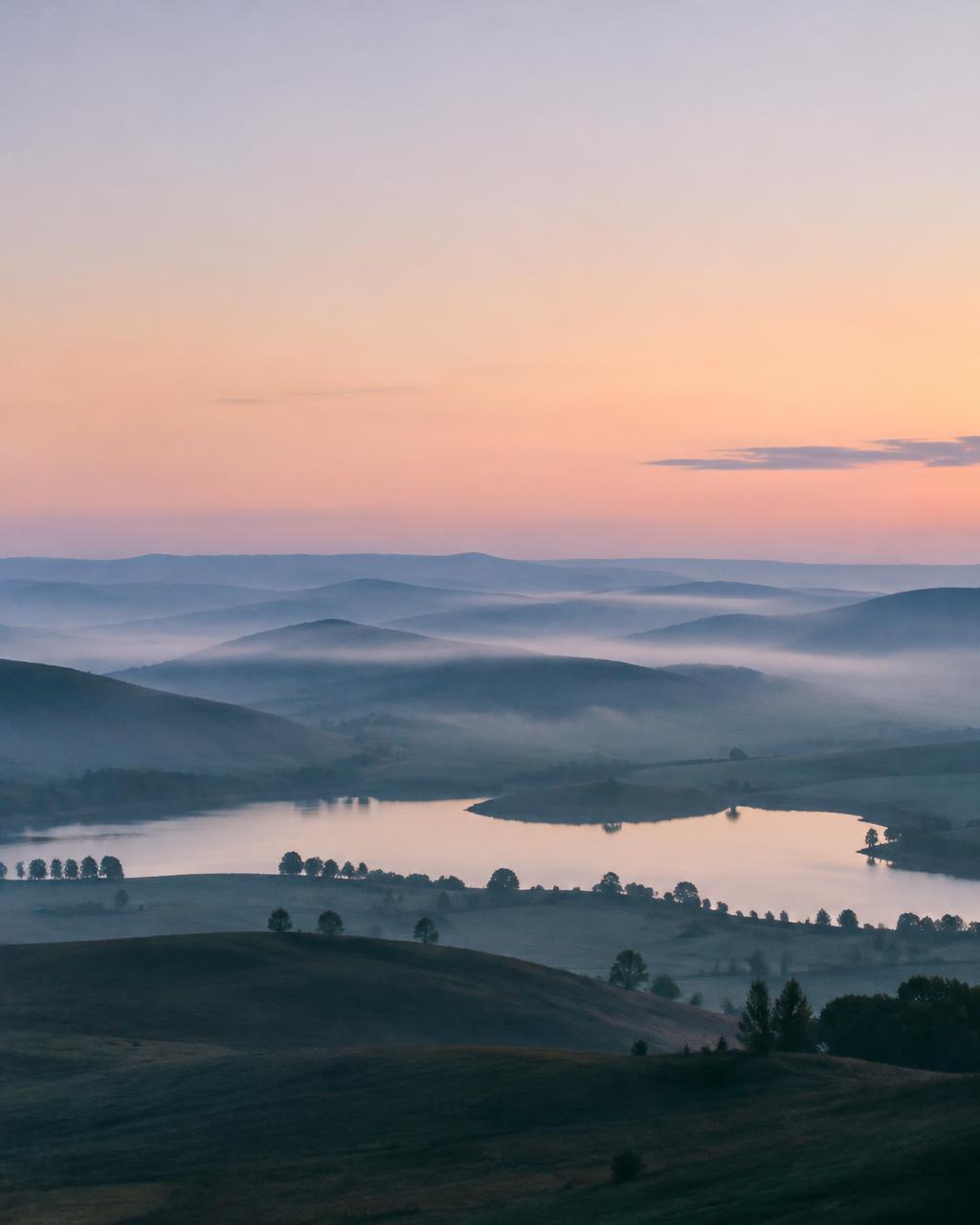 Pastel dawn over misty hills and a lake